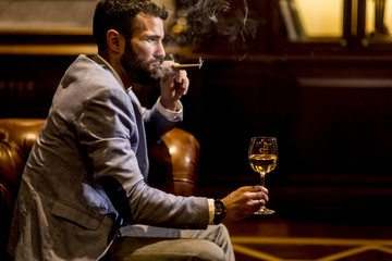 Young man tasting white wine and smoking cigar