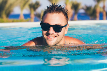 portrait of a young, handsome man who bathes in the pool in the summer, in the background of green trees, he was smiling, wearing sunglasses