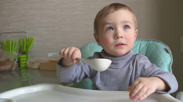 Happy child eating porridge with a big spoon