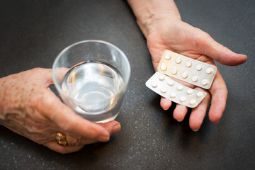 Close up of old hands with tablets and a glass of water.