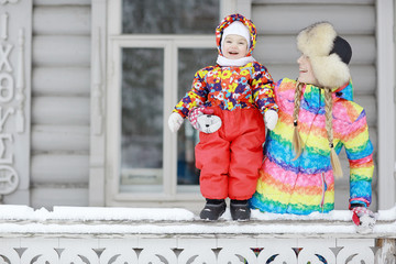 Fototapeta na wymiar young woman and a young child in a bright colored clothing playing in the winter snow