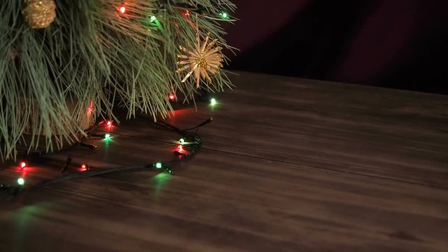 The man puts gift boxes under the Christmas tree. Fir stand on the wooden table, decorated glowing garland and Christmas toys. Boxes with gift wrapped in brown and colored paper and tied with twine.