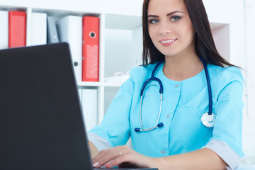 Young female medicine doctor sitting at the table and working at the laptop.