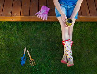 Woman with cup of coffee sitting on a patio wooden deck resting after working in the garden