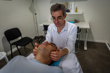 A mature therapist places his hands on the sides of a man's face