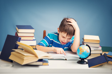 seven years old child reading a book at home. Boy studing at table on blue background