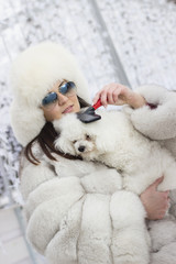 Fototapeta premium Winter time fun. Woman wearing fur hat and winter coat holding her dog while she is grooming him. Brushing the dog in the winter time.