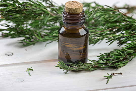 Rosemary essential oil on a  bottle with  fresh rosemary on wooden background, selective focus.