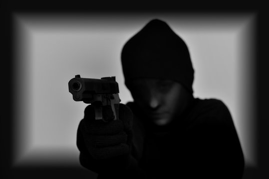 Female robber with black tights over her head holding a gun and aiming. Black and white. Low key. Selective focus.  