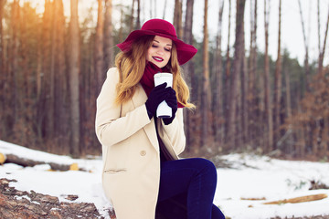 Young, beautiful and stylish red hair girl in coat and hat keeps a thermo cup. Fashion.
