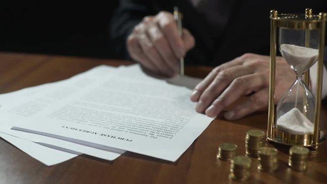 Serious businessman signing purchase agreement as time flows with sand in clock