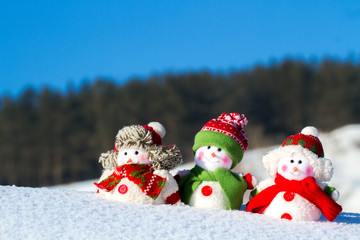 The winter, Christmas - three happy snowmen stand against the background of the blue sky.