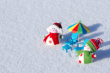 Two cute snowman sunbathing in the snow. Paper beach chairs and a  umbrella. Winter background
