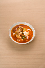 Italian fish soup with salmon, shrimps and vegetables in white dish. On striped wooden background.