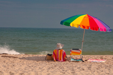 Colorful Beach Umbrella and Woman in Chair at Shore