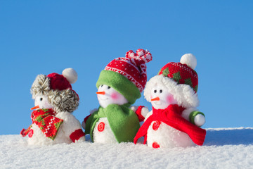 The winter, Christmas - three happy snowmen stand against the background of the blue sky.