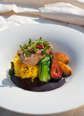 Smoked pork fillet with caramelized apples, figs, garlic potatoes, and red wine sauce. On white plate and restaurant table.