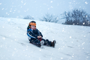 Fototapeta na wymiar Cute little boy with saucer sleds outdoors on winter day. Excited child sledding down a hill.