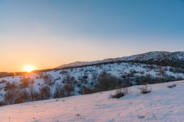 The orange sun sets over the snow-covered mountain. Russia, Stary Krym. - obrazy, fototapety, plakaty
