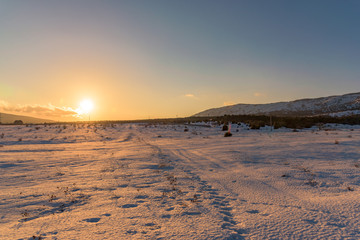 Amazing orange sunset in snow-covered field with footprints. Russia, Stary Krym.