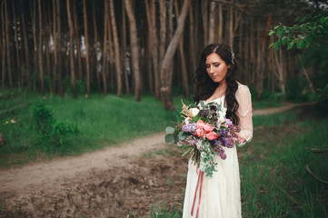 Beautiful bride in the forest with a large bouquet of different flowers. Boho style