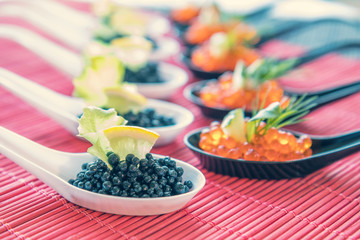 Fototapeta premium Delicious red and black caviar fish close-up in white and black spoons on white table. Beautifully decorated catering banquet table.