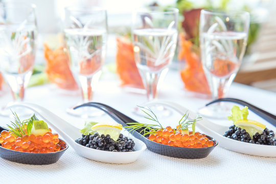 Delicious red and black caviar fish close-up in white and black spoons on white table. Beautifully decorated catering banquet table.