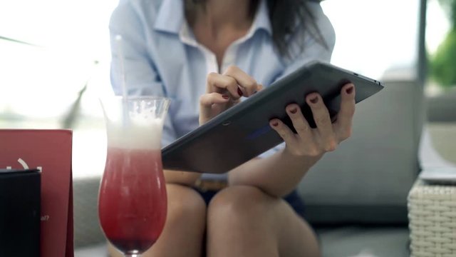 Young, elegant woman using tablet while sitting in cafe in city, focus on hands, 4K
