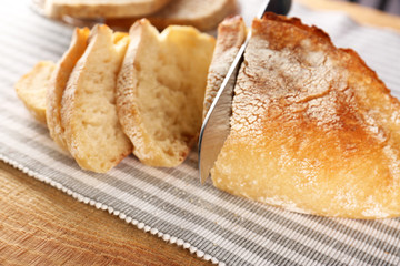 Slicing of fresh bread with knife on fabric closeup