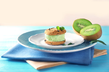 Plate with delicious ice cream cookie sandwich and kiwi on napkin