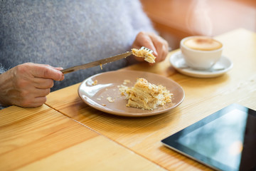 Hands and piece of cake. Tablet on wood table.