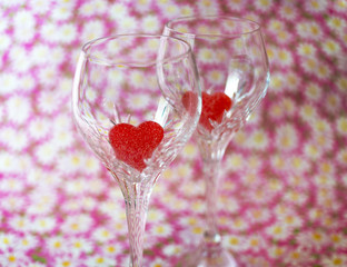 Two crystal wine glasses with vibrant red heart shaped candies i
