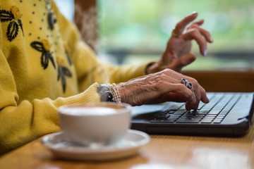 Senior woman's hands and keyboard. Notebook pc and cup. Learn to type fast.