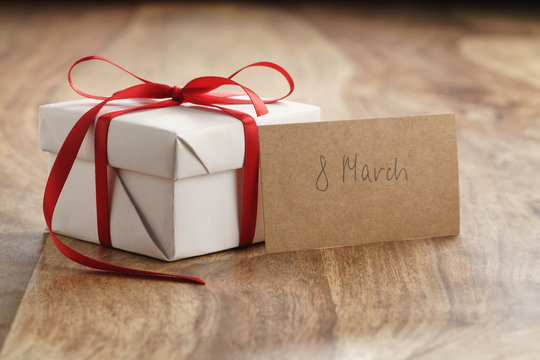 white paper gift box with thin red ribbon and 8 march paper card on old wood table, shallow focus