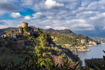 Obraz premium Rocky coastline with medieval castle ruins on hill near Portofino town, Italy 