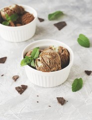 chocolate mint ice cream in white bowls with pieces of chocolate and mint leaves on a marble table