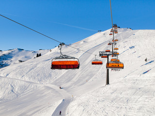 Chair ski lift with orange bubble shelter on sunny winter day. White snow and clear blue sky in Saalbach Hinterglemm Leogang Resort, Austria, Alps, Europe.