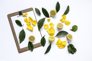 Clipboard with and lemons and Petals of yellow rose on black bac