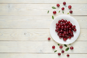 ripe cherries and leaves in a dish on a textured wooden background, view from above