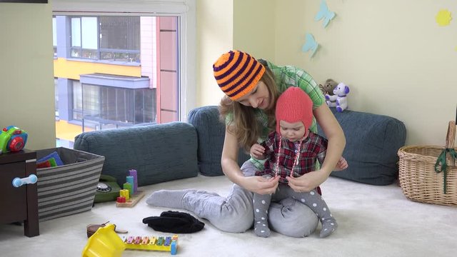 Mother with cute baby girl measure colorful knitted hats between toys