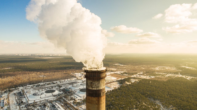 Heat electric station in winter. Aerial view. From above. Power station in a forest in sunny weather. Pipe with smoke close up