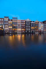 Fototapeta na wymiar Houses facades over canal with reflections illuminated at blue night, Amsterdam, Netherlands