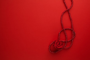 Decorative rose and beads on red background. Flat lay