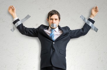 Businessman in suit is taped to the wall with adhesive tape.