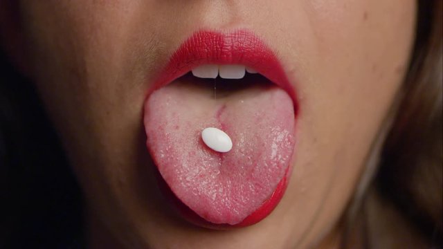Woman in red lipstick reveals a white pill on her tongue, then swallows it.