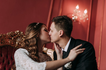 cute wedding couple in the interior of a classic studio with red background . hey kiss and hug each other, holding hands looking at each other