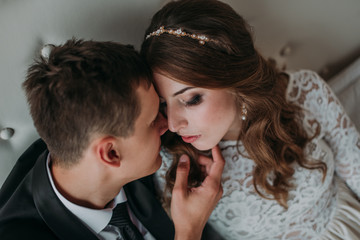 cute wedding couple in the interior of a classic white studio decorated. hey kiss and hug each other, holding hands looking at each other