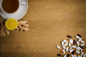 Choose between the traditional and folk medicine. Cup of tea, lemon, ginger, different pills on wooden background. Top view. Copy space. Health concept.
