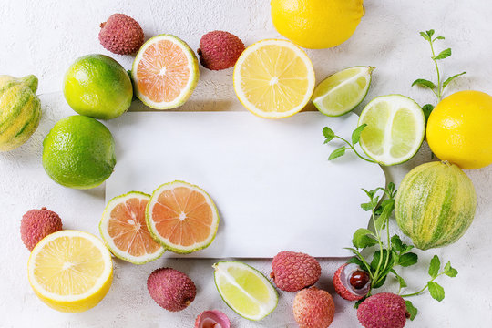 Variety of whole and sliced citrus fruits pink tiger lemon, lemon, lime, mint and lichee with empty cutting board over white concrete textured background. Top view, space for text, healthy eating