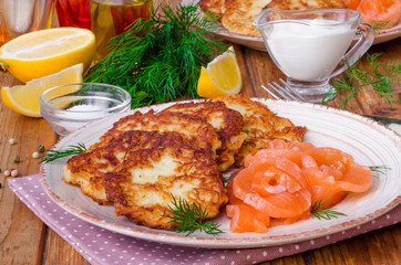 Potato pancakes with sour cream and salmon on a plate on a wooden background
